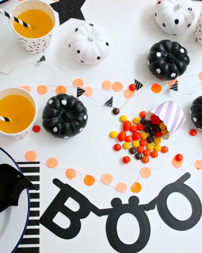 Black and white table with Boo garland, polka dot pumpkins, candy and striped cups