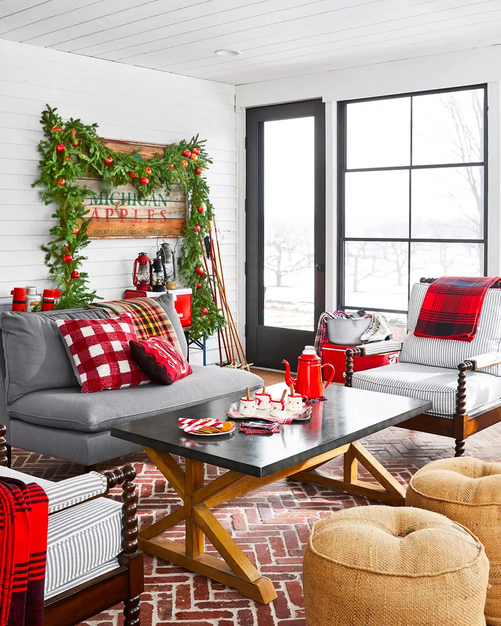 White shiplap living room with gray sofa, red check pillows, a garland and woven poufs