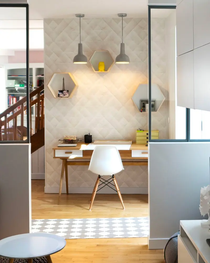 Small office nook with wood desk, white molded chair, hexagon shelves and two gray pendant lights