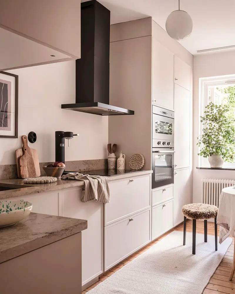 Taupe kitchen with black range hood, concrete counters, built-in oven and upholstered stool
