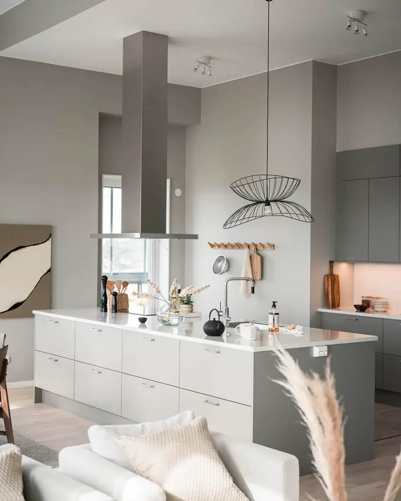 Gray kitchen island with stainless hood, wire pendant light, pampas grass and white sofa in front
