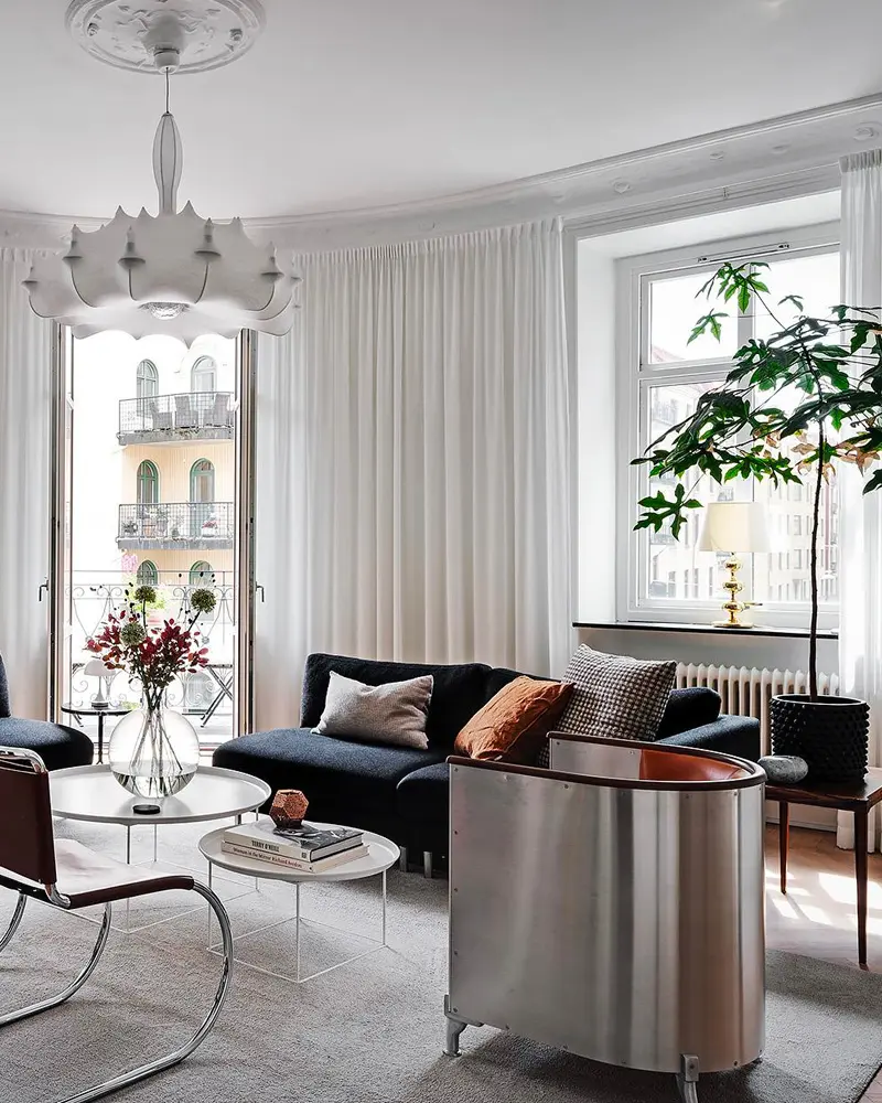 Dark sofa with rust pillows, steel side table and feather pendant by sheer curtains