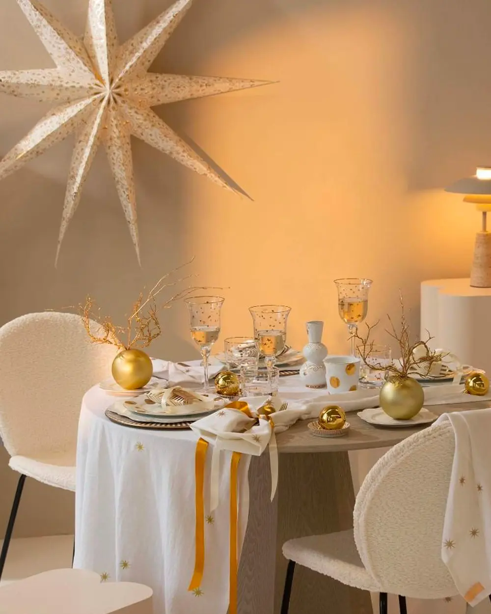 Round white dining table with gold baubles, gold-rimmed glasses and a large paper star overhead