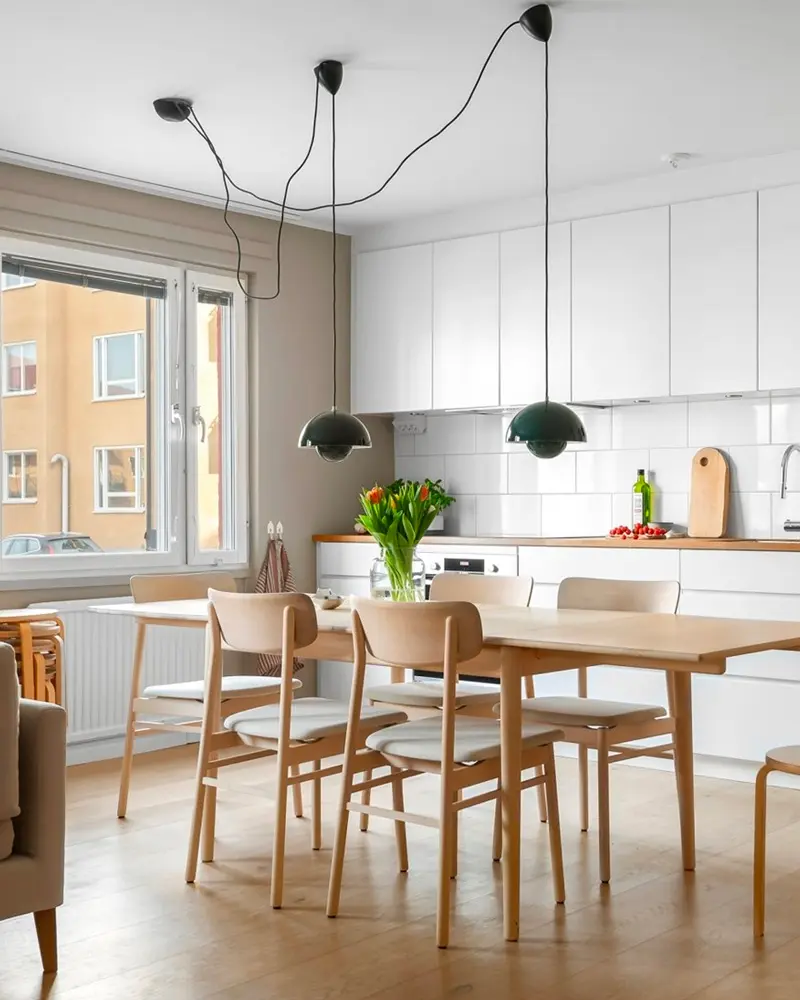 Wood dining table and chairs in a white kitchen with three dark pendant lights and tulips