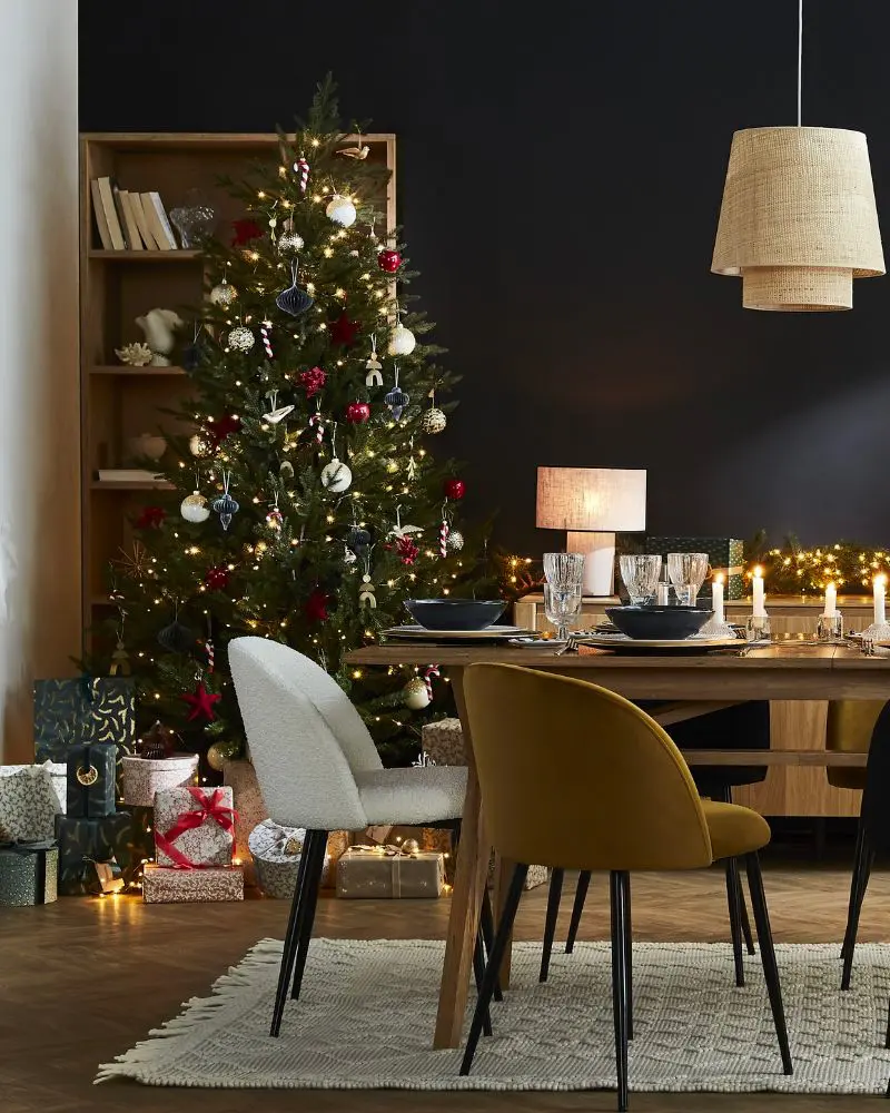 Dark dining room with lit tree, mustard velvet chair and rattan pendant