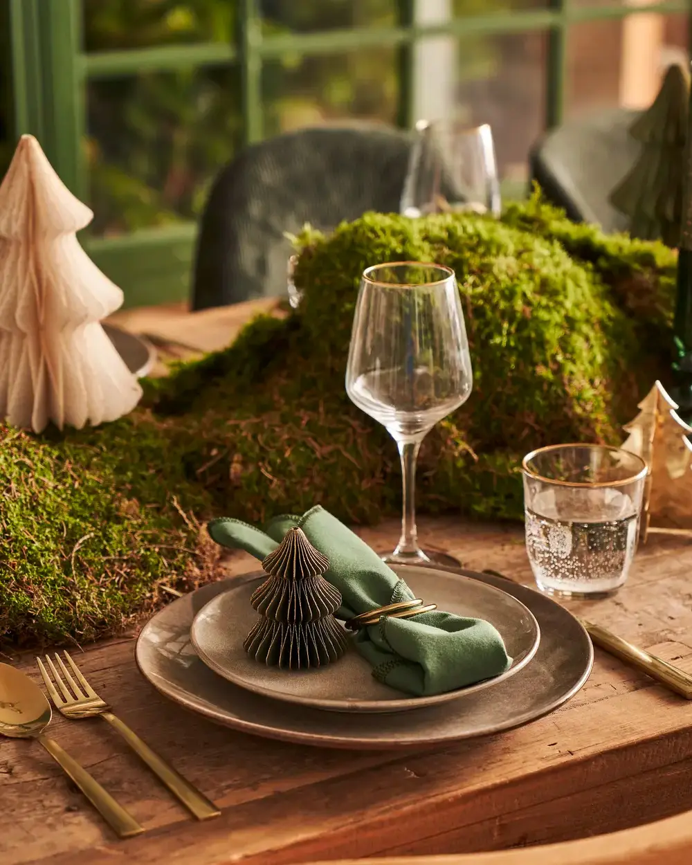 Place setting on a bed of moss with a paper tree on the plate, green napkin and wine glass