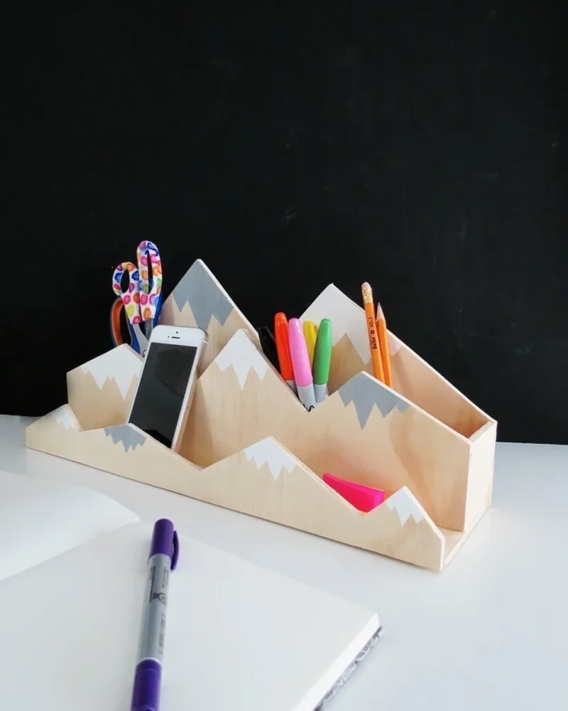 Wooden mountain-shaped desk organizer with snowy peaks holding pens and phone