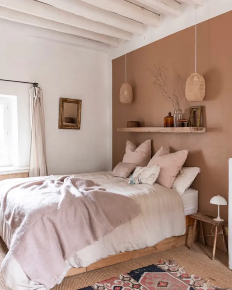 Bedroom with a terracotta-pink accent wall, pink bedding and rattan pendants
