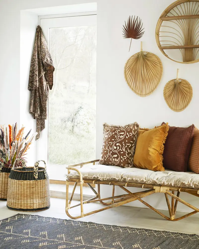 Rattan daybed with mustard and brown pillows, woven palm fan wall decor and baskets