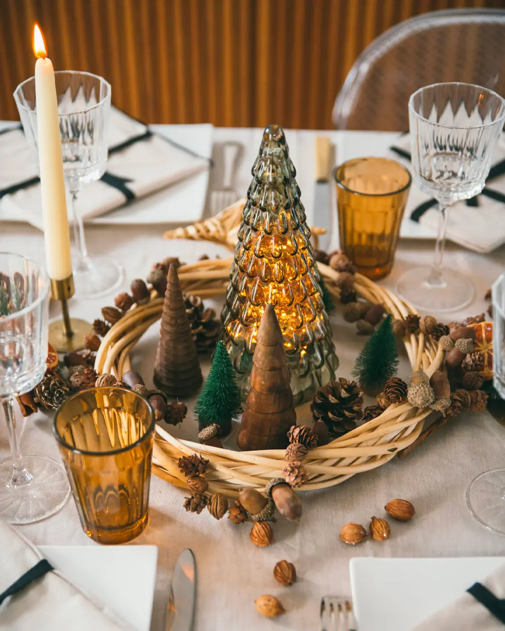 Christmas centerpiece with a wicker wreath, pinecones, small glass trees, amber glasses and a taper candle