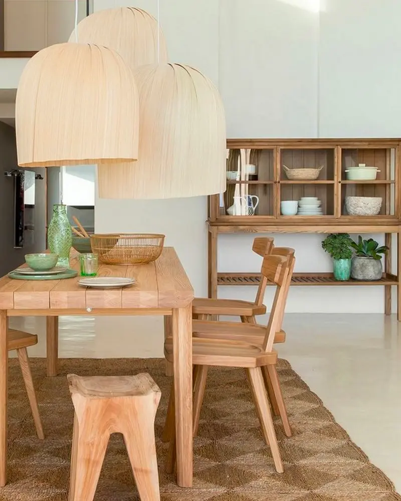 Light wood dining table, chairs and stool under oversized wood-veneer pendants