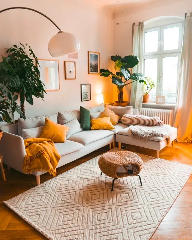 Gray sectional with mustard pillows, diamond-pattern rug, rattan pouf and big plants