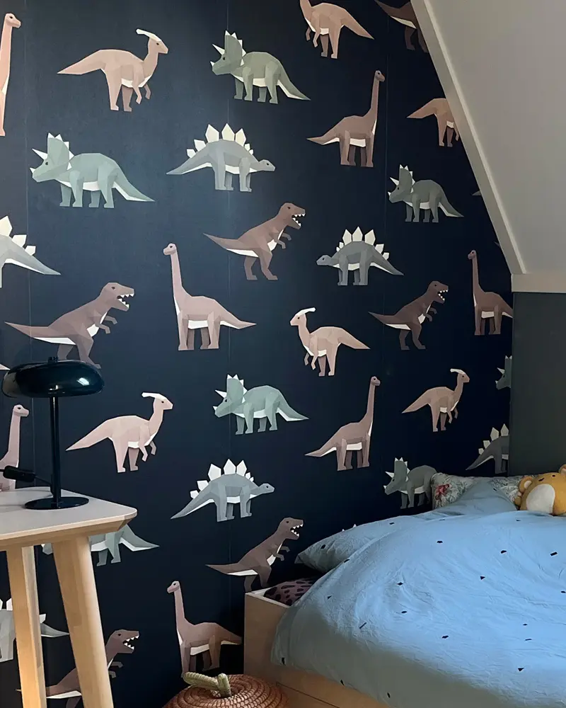 Navy wallpaper with beige and sage dinosaurs behind a bed with a blue duvet