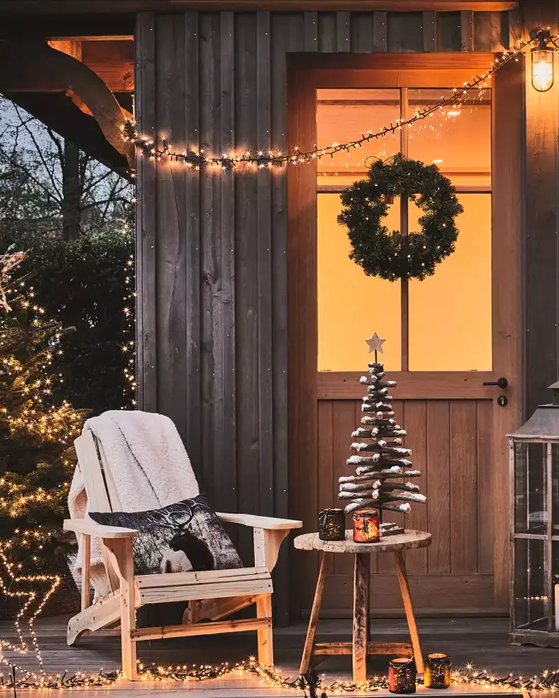 Dark wood porch with a lit wreath on the door, Adirondack chair and string lights