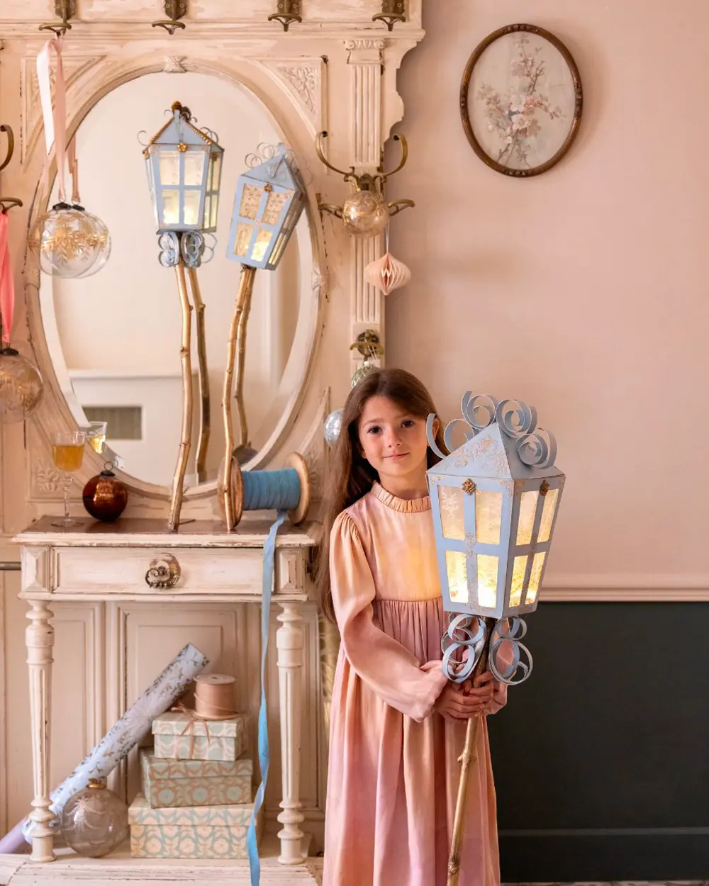 Girl holding a large blue paper street lantern with a glowing light in a pink room