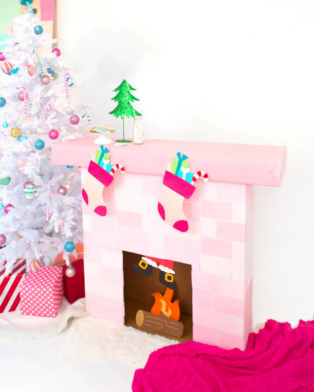 Pink cardboard brick fireplace with paper fire, stockings and a small glitter tree beside a white tree