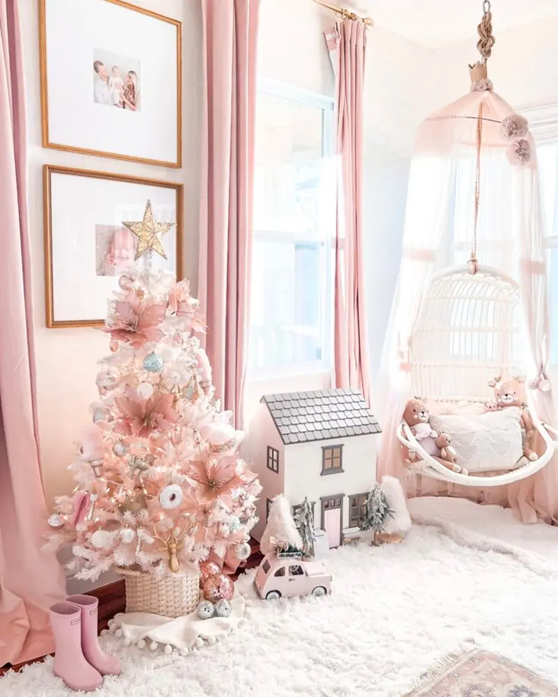 Pale pink bedroom with a small blush Christmas tree, a white dollhouse and a hanging rattan chair on a fluffy rug