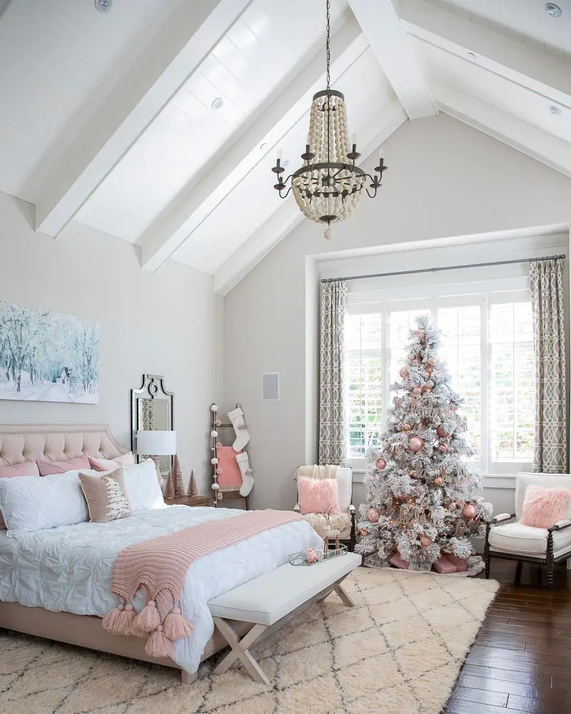 Bright bedroom with vaulted ceiling, crystal chandelier, flocked Christmas tree and pink bedding with a pink throw on a bench