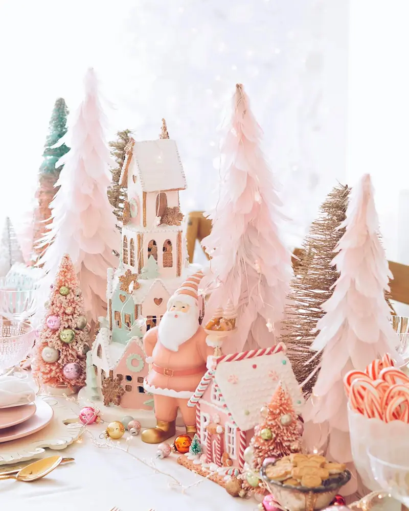 Table centerpiece of pale pink feather trees, gingerbread houses and a vintage Santa figurine