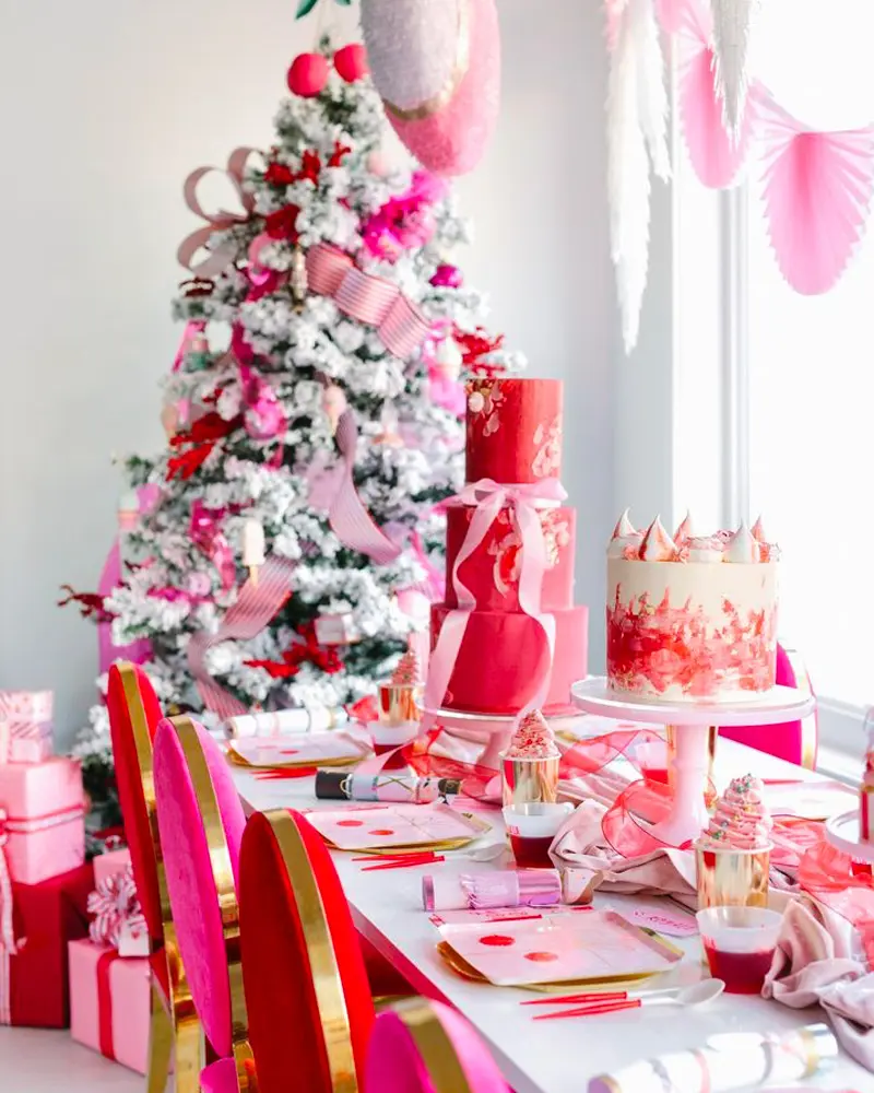 Festive dining table in pink, red and white with red chairs, a red layer cake and a flocked tree with pink and red ornaments