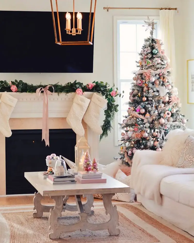 Living room with a green garland and pink ribbons on the mantel, cream stockings, a coffee table and a decorated tree