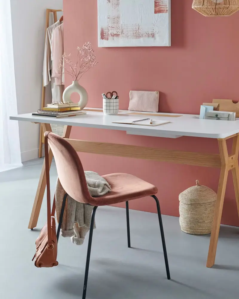 Dusty pink wall with white and wood desk, pink velvet chair on black legs and woven basket