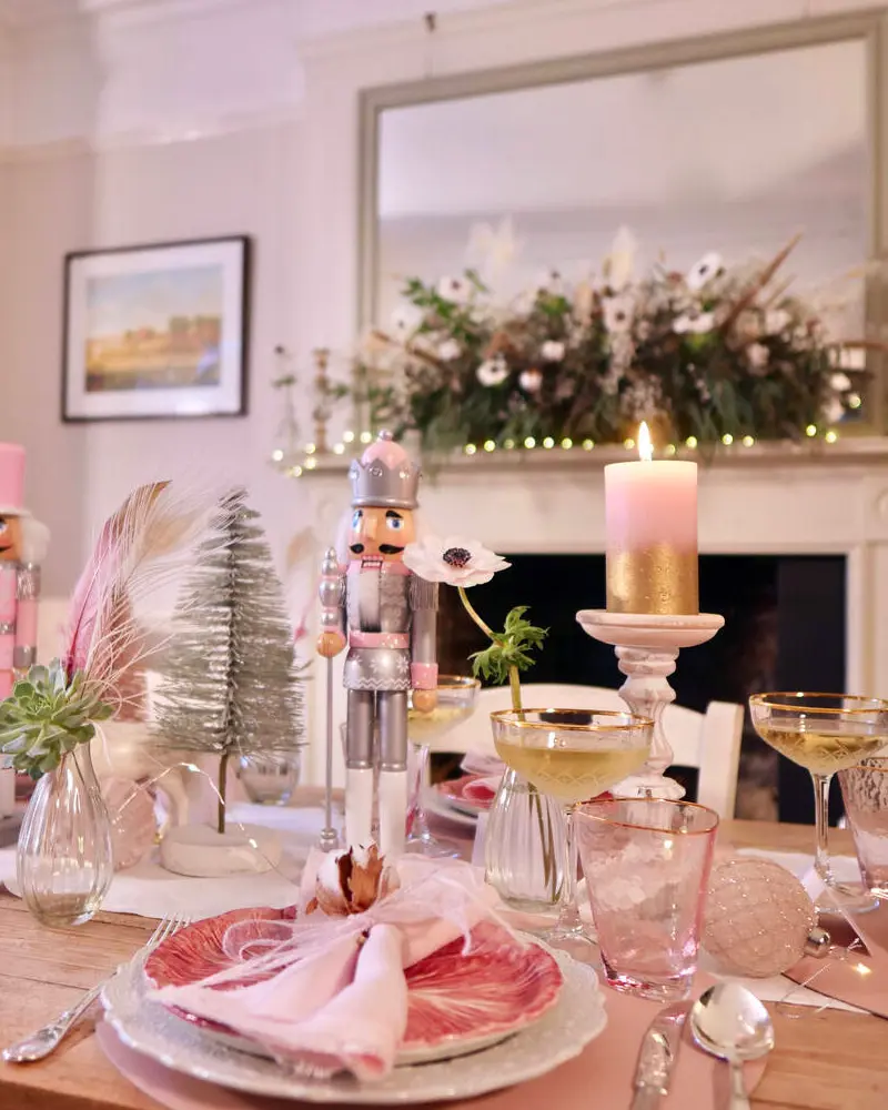 Holiday table with pink napkins, a nutcracker, champagne coupes, a pink pillar candle and a small bottle-brush tree