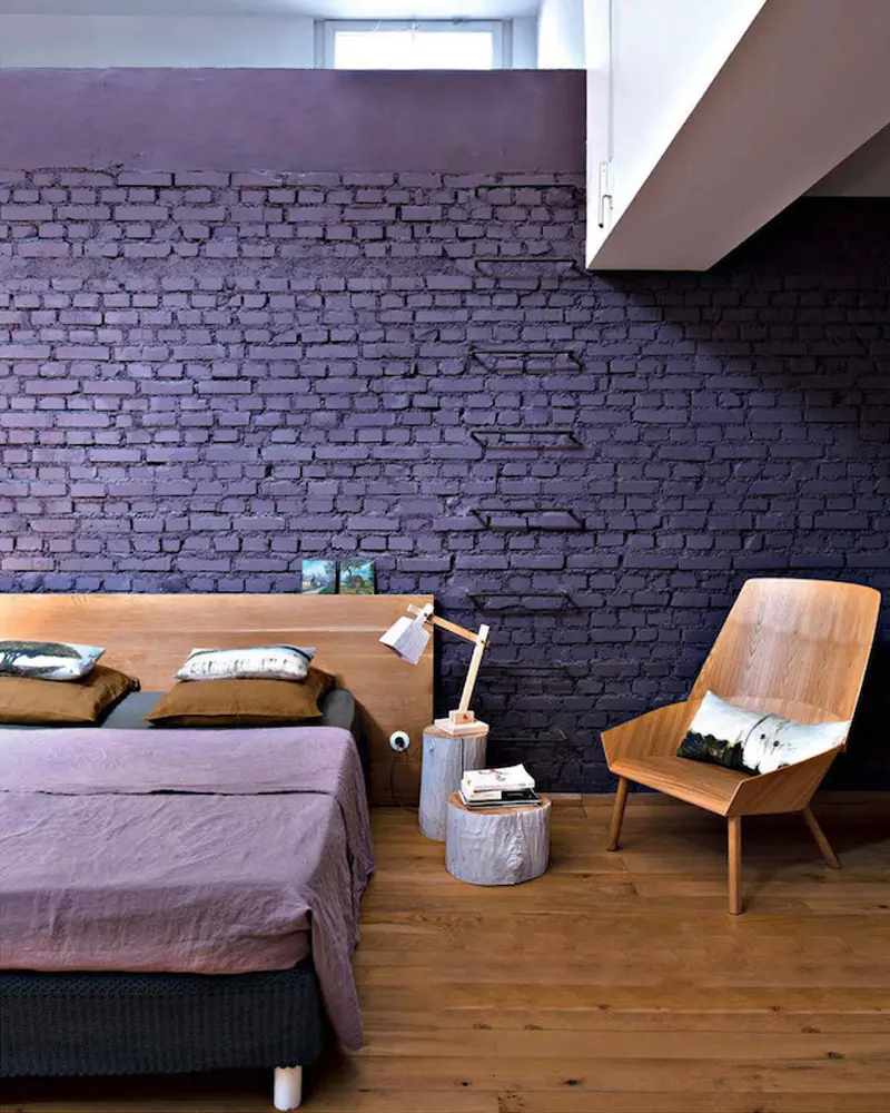 Bedroom with a purple painted brick wall, wood headboard and plywood armchair