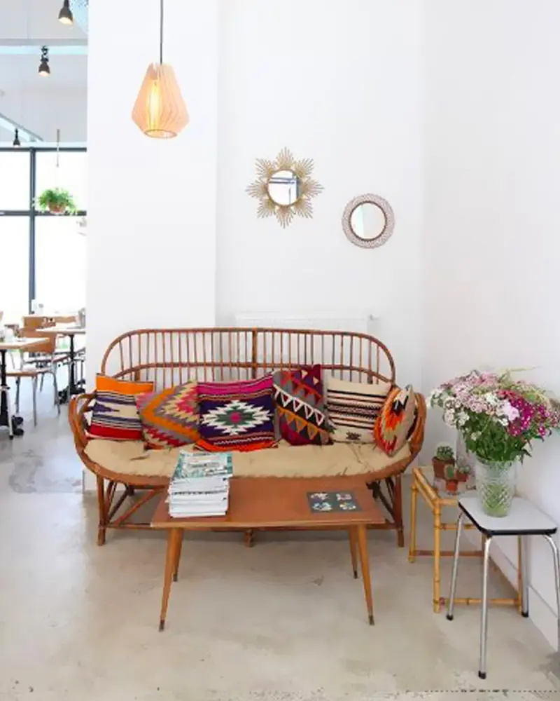 Small vintage rattan sofa with kilim pillows, wood coffee table, sun mirror and flowers