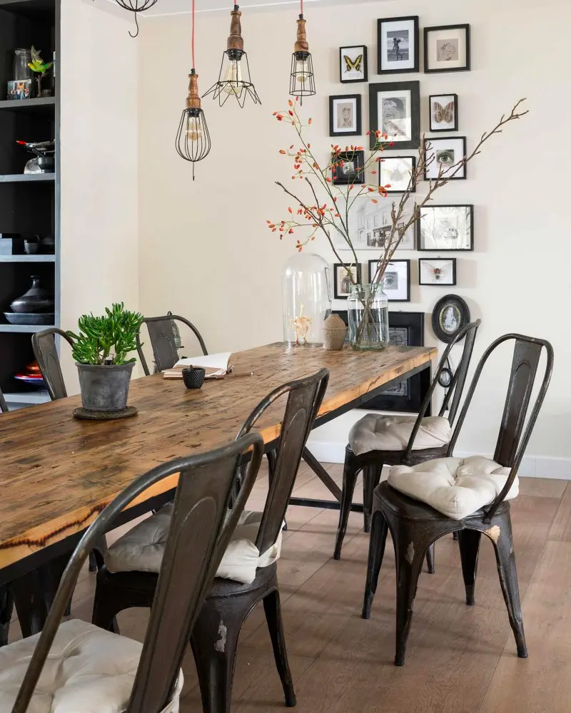 Long reclaimed wood dining table with black metal chairs, cage pendants and a frame gallery wall