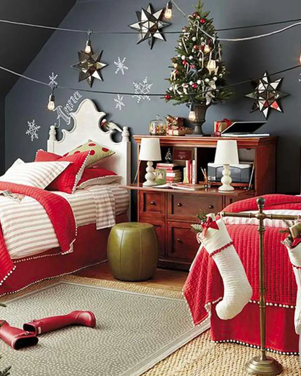 Bedroom with red bedding, white stockings, a small tree on a desk and paper stars on a dark wall