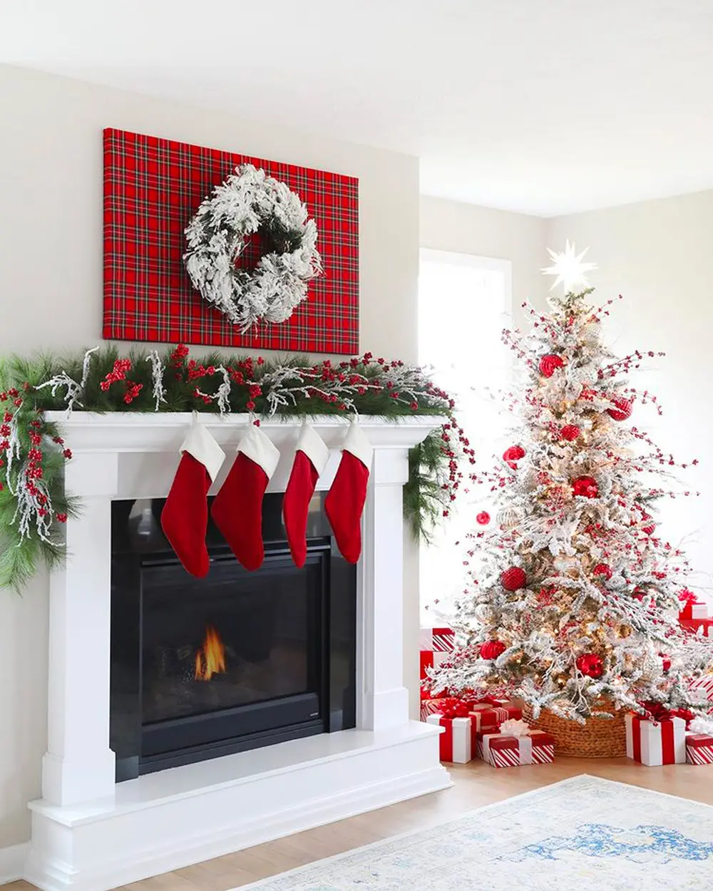 White fireplace with four red stockings, a flocked garland with red berries and a wreath on red plaid