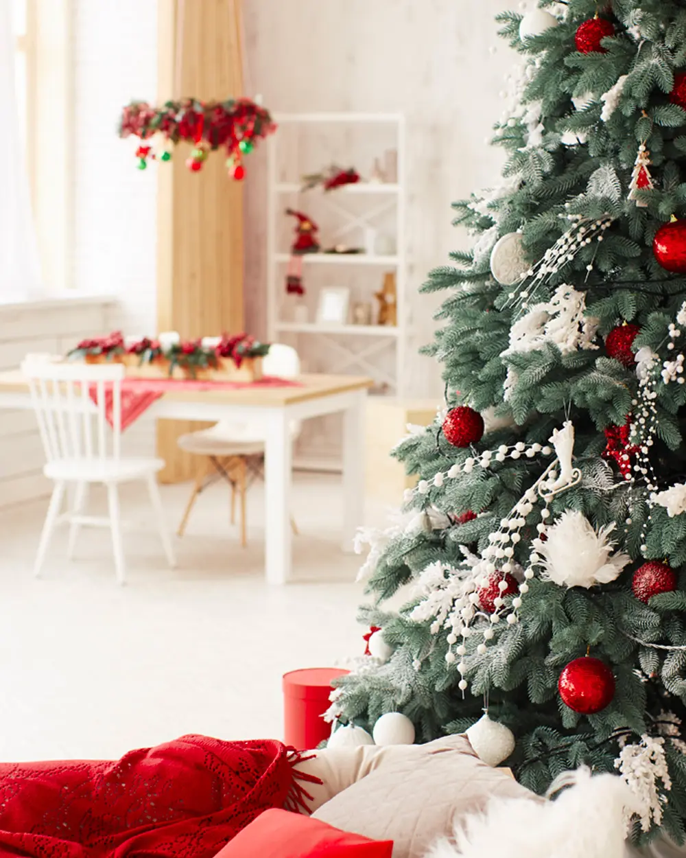 Close-up of a tree with red and white ornaments in front of a white dining nook with red accents