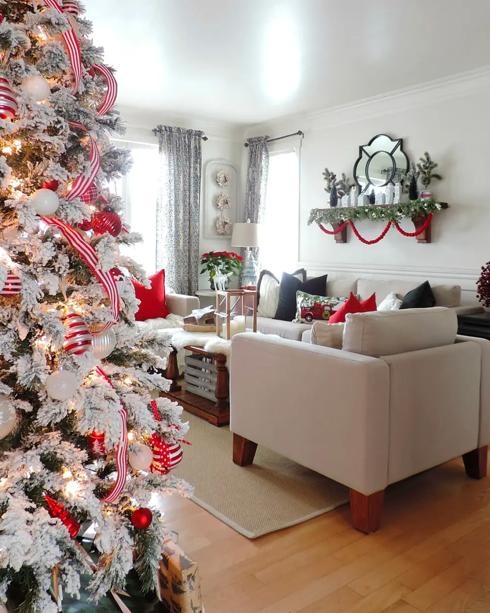 Flocked white tree wrapped in red and white striped ribbon beside a neutral living room