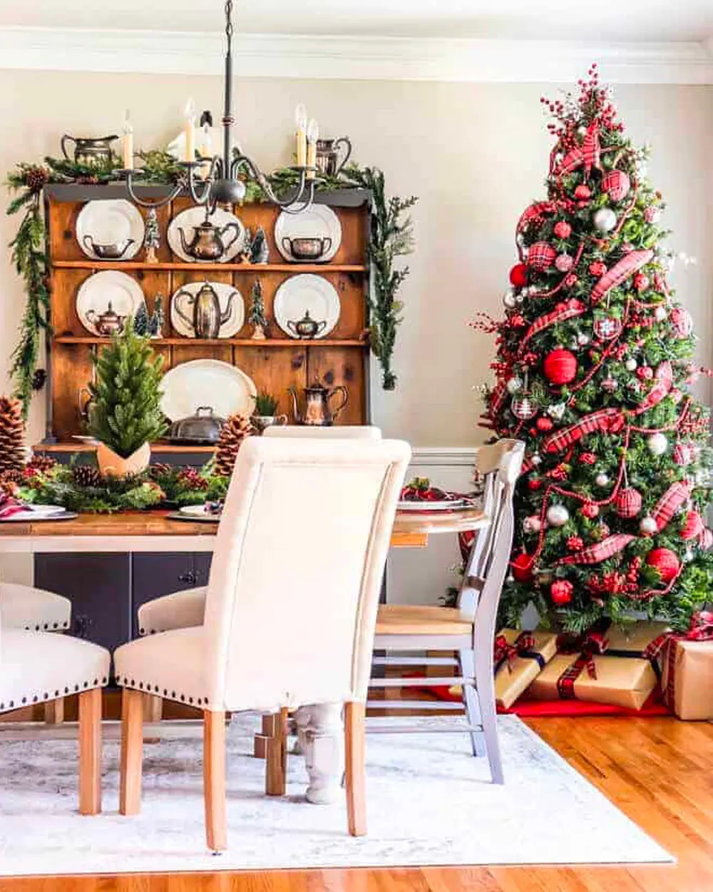 Dining room with a wooden hutch, white chairs, a garland and a red and white decorated tree