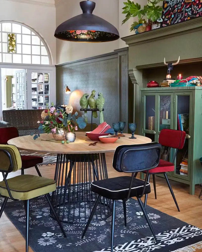 Eclectic dining room with olive walls, green cabinet and mismatched colorful chairs
