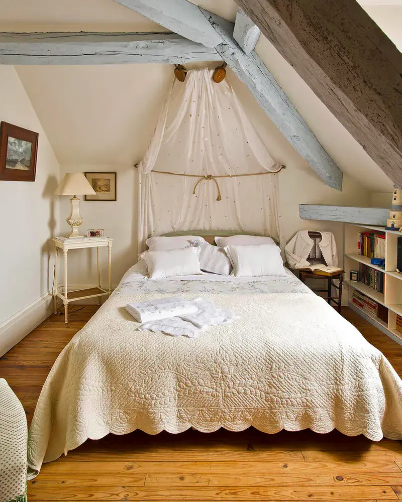 Attic bedroom with a white lace canopy, a scalloped white bedspread and pale blue beams