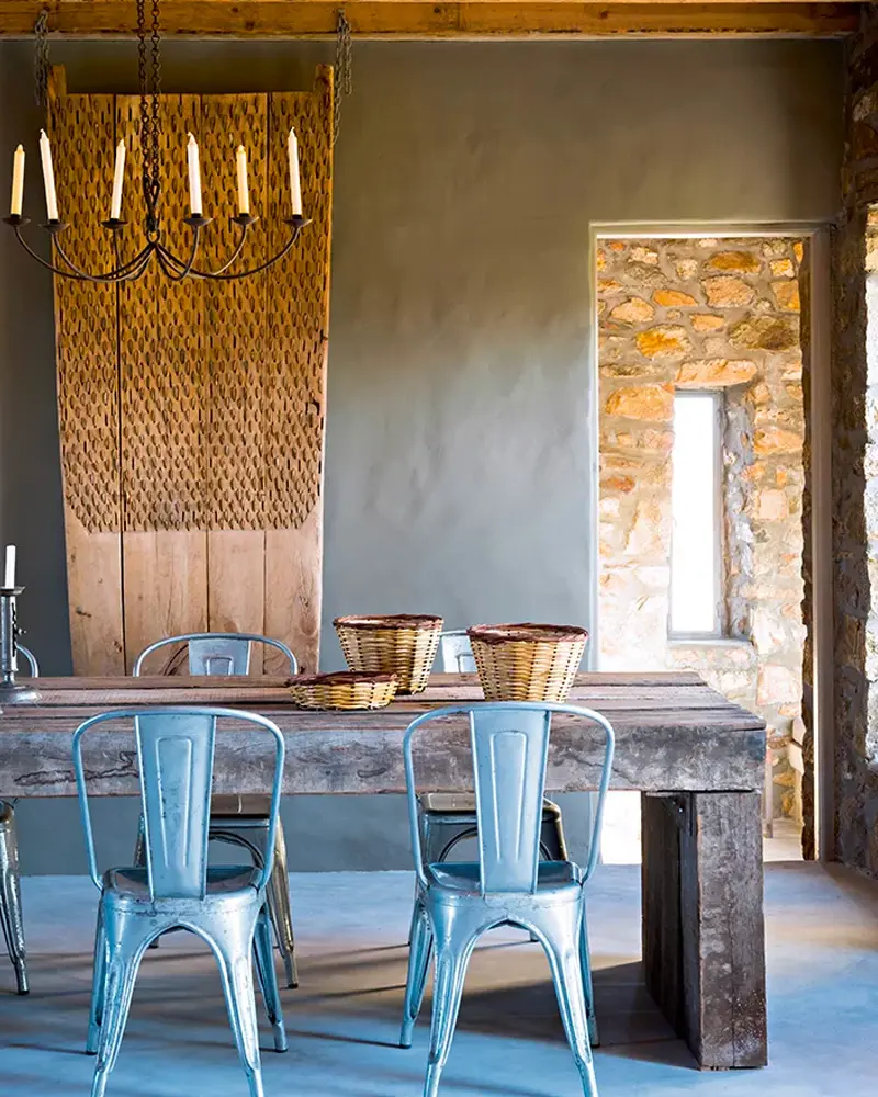 Chunky wood table with light blue metal chairs, wicker baskets and a stone wall