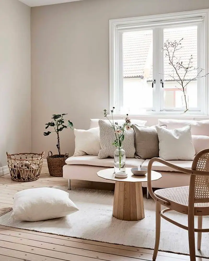 Scandinavian living room with a pale pink sofa, beige pillows, a round wood pedestal table, a bentwood cane chair and a basket of plants