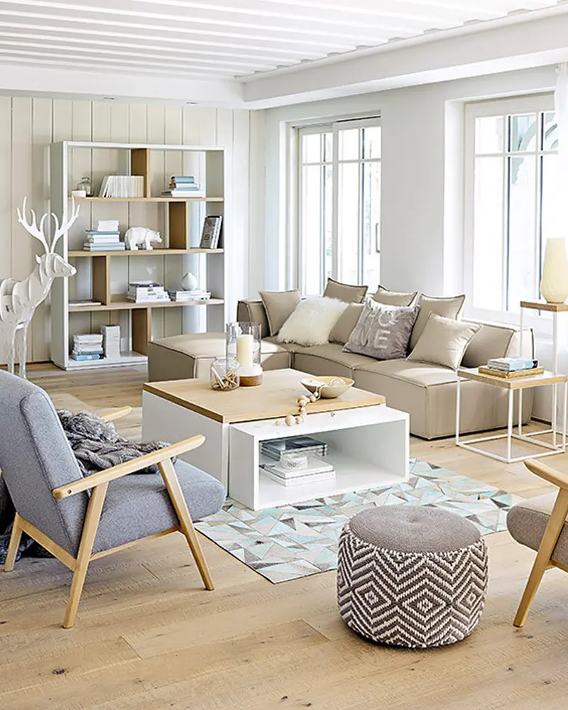 Scandinavian living room with a beige sofa, a white and wood coffee table, a gray armchair, a patterned pouf and open white shelving