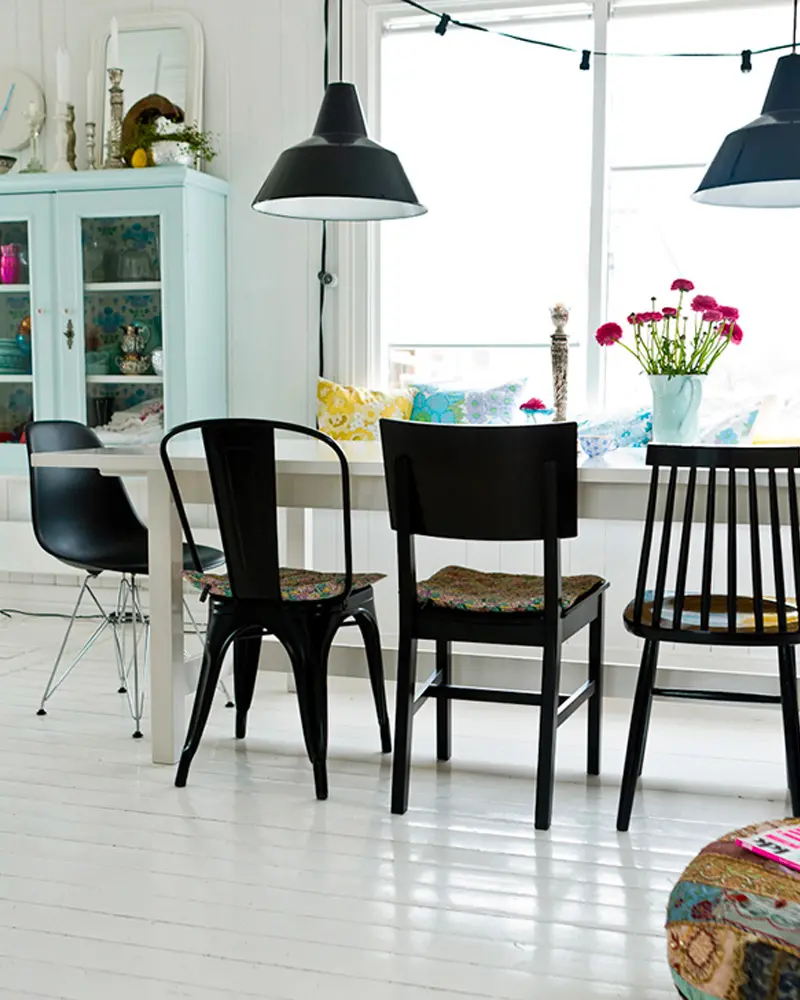 White dining table with mismatched black chairs and black enamel pendant lights