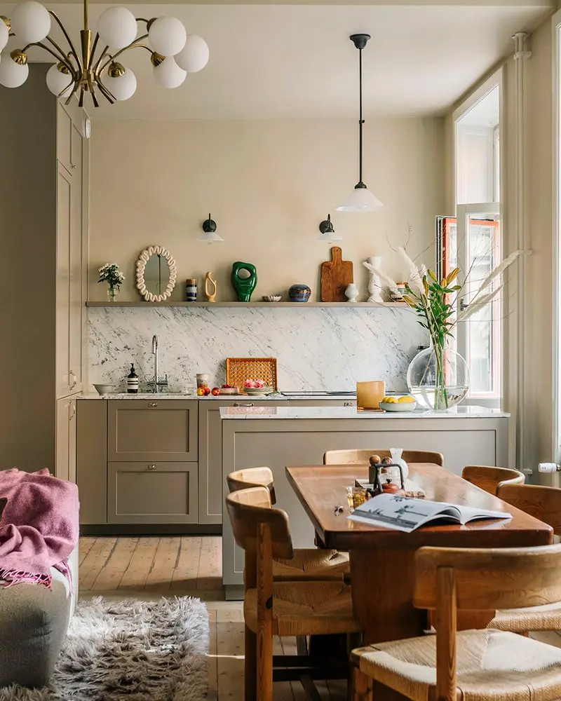 Olive cabinets with marble backsplash, wood shelf with ceramics, globe chandelier and wood dining table