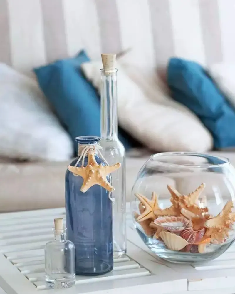 Close-up of a glass bottle with starfish and a bowl of shells by blue pillows