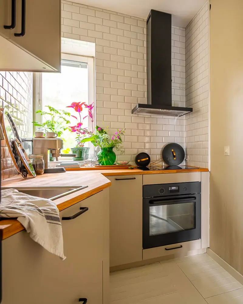 Small beige kitchen with white subway tile, black range hood, wood counter and pink flowers