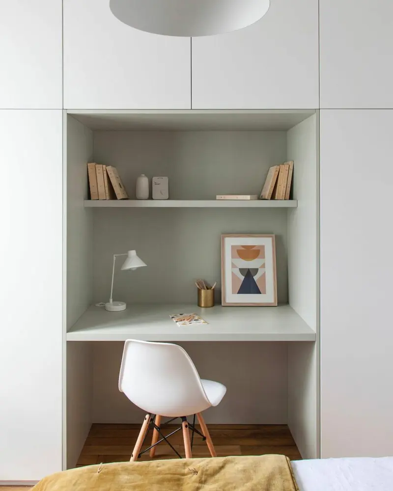 Desk niche built into a wall of white wardrobes with sage green interior