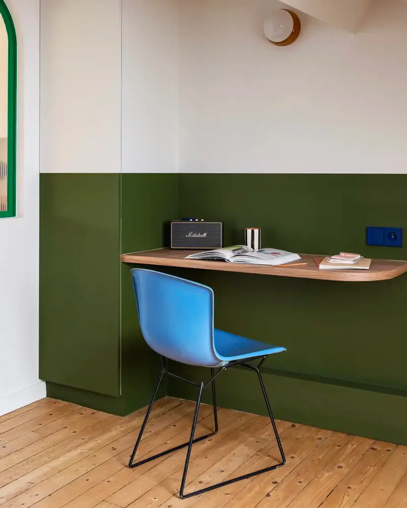 Wood desk shelf on a two-tone green wall with a blue wire chair
