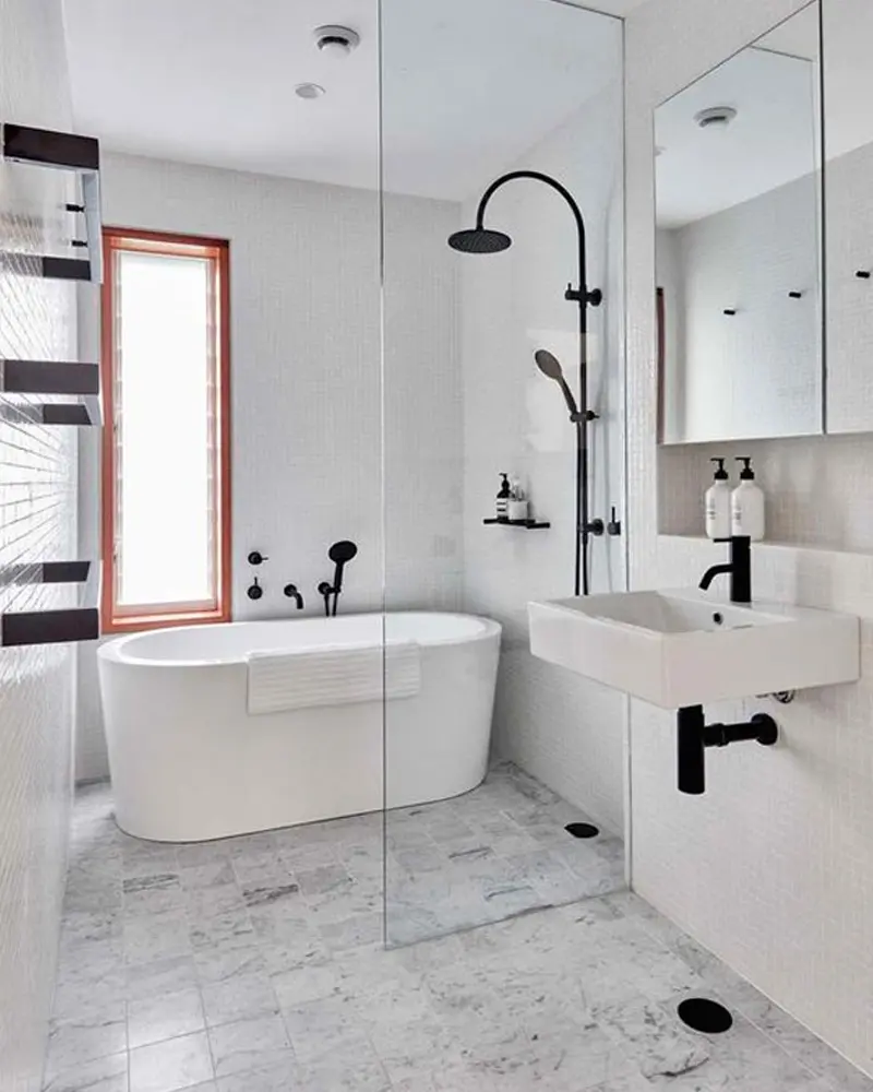 White bathroom with freestanding tub, black shower fixtures, wall-hung sink and terracotta window frame