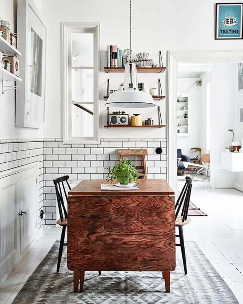 Small dining nook with subway tile, rustic wood table, black chairs and white pendant