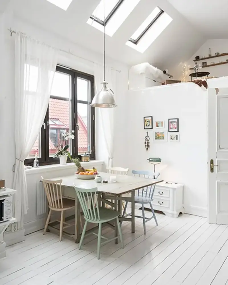White attic dining room with skylights, pastel spindle chairs and metal pendant