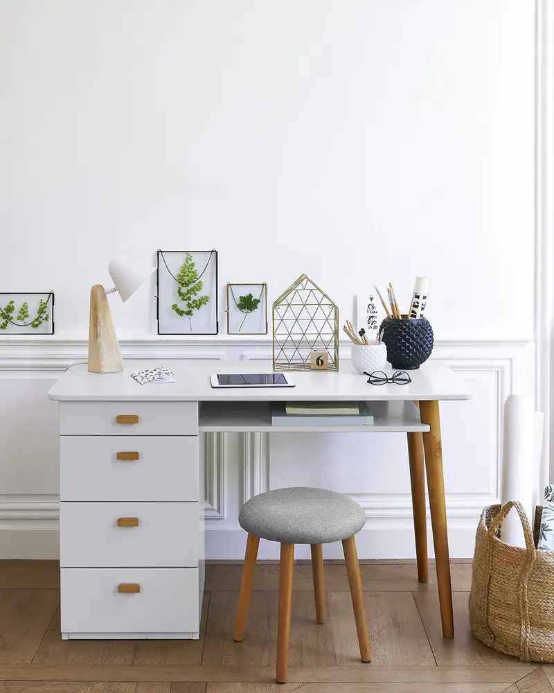 White desk with drawers, gray upholstered stool, pressed-leaf frames and woven basket